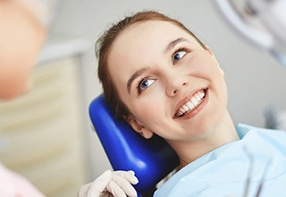 Young woman in dental chair smiling up at her dentist