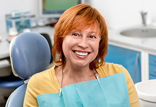 Smiling senior woman in dental chair looking at her smile in mirror after receiving dental services in Inver Grove Heights