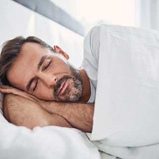 Bearded man lying on side and sleeping soundly in bed